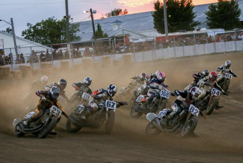 Dirt track with a fence in the background and motorcycles racing in the dirt